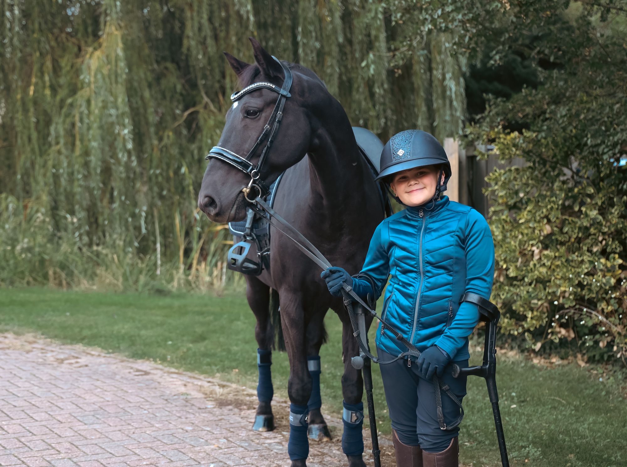 A young rider on crutches standing with his bay pony