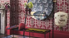 Wall decorated with bright pink chinese style wallpaper and pink skirting board, dark wooden flooring, a colourful rug and black metal bench