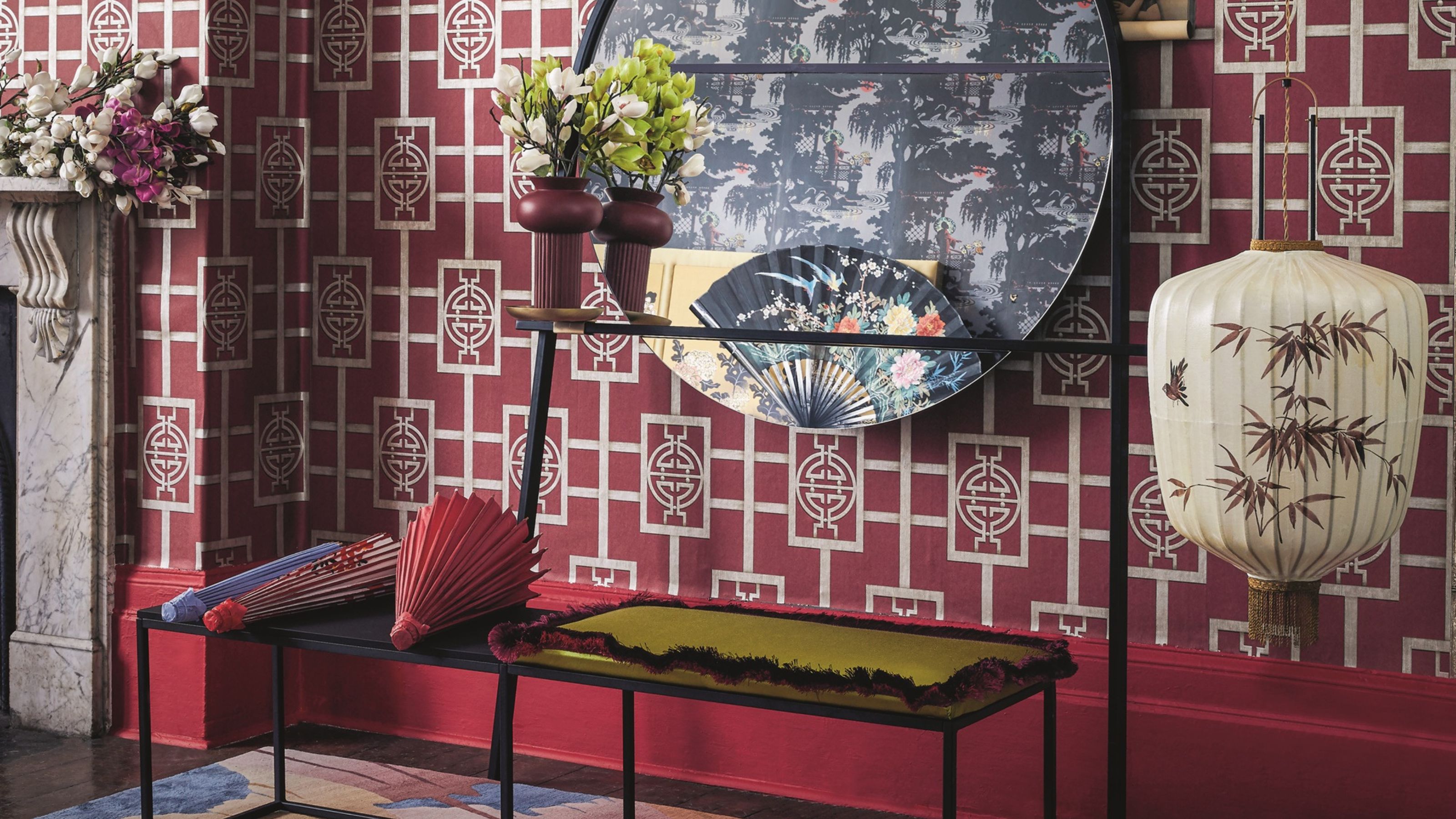 Wall decorated with bright pink chinese style wallpaper and pink skirting board, dark wooden flooring, a colourful rug and black metal bench