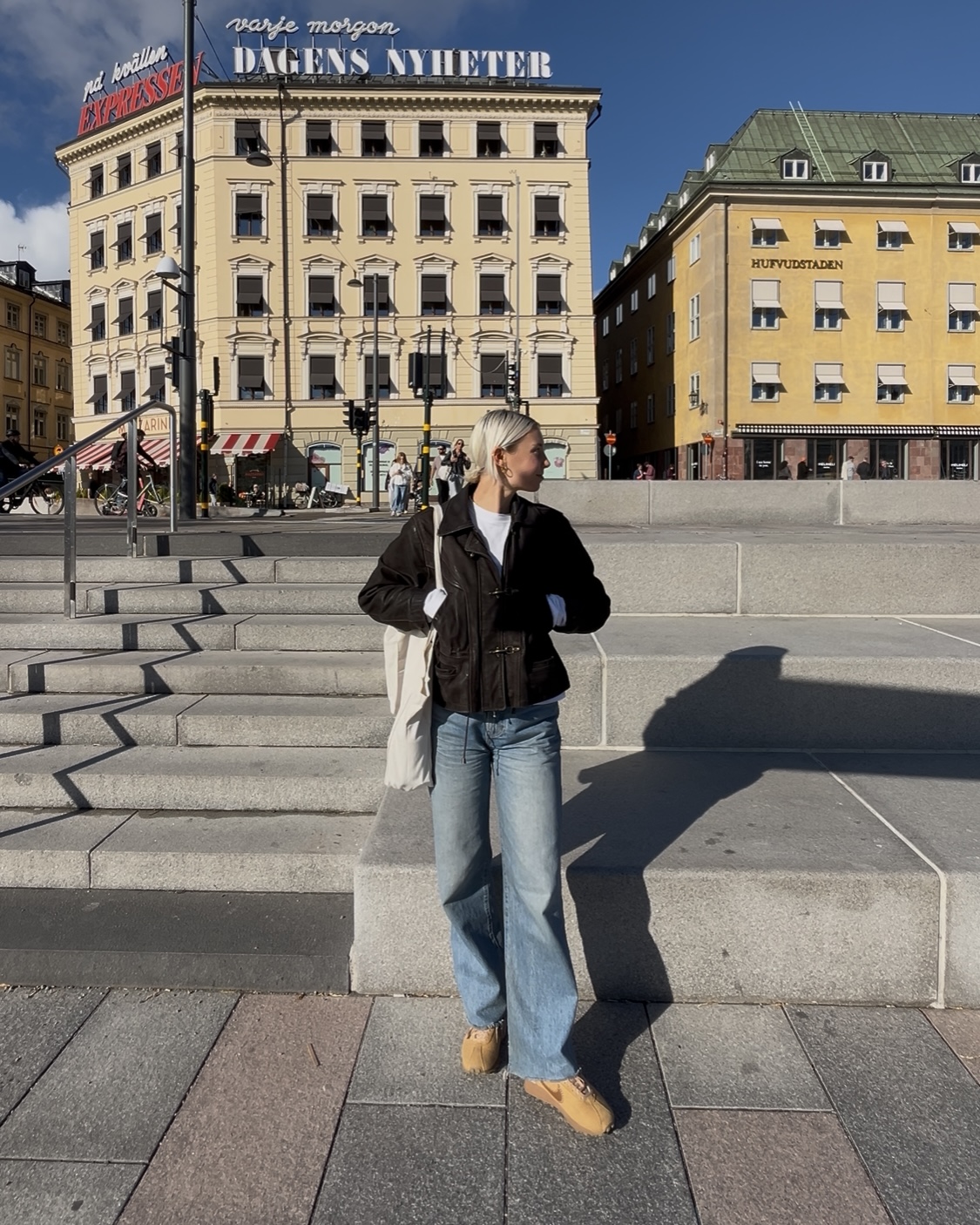 A woman standing in Stockholm&#039;s Old Town wearing jeans and a brown jacket