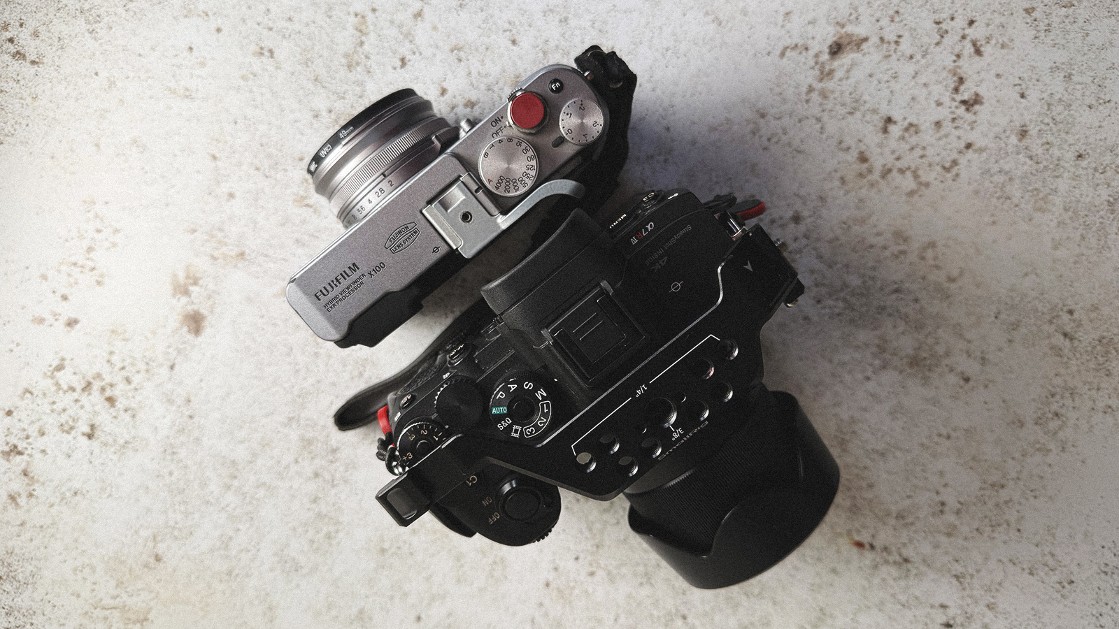 A Fujifilm X100 and a Sony A7Riv on a table top.