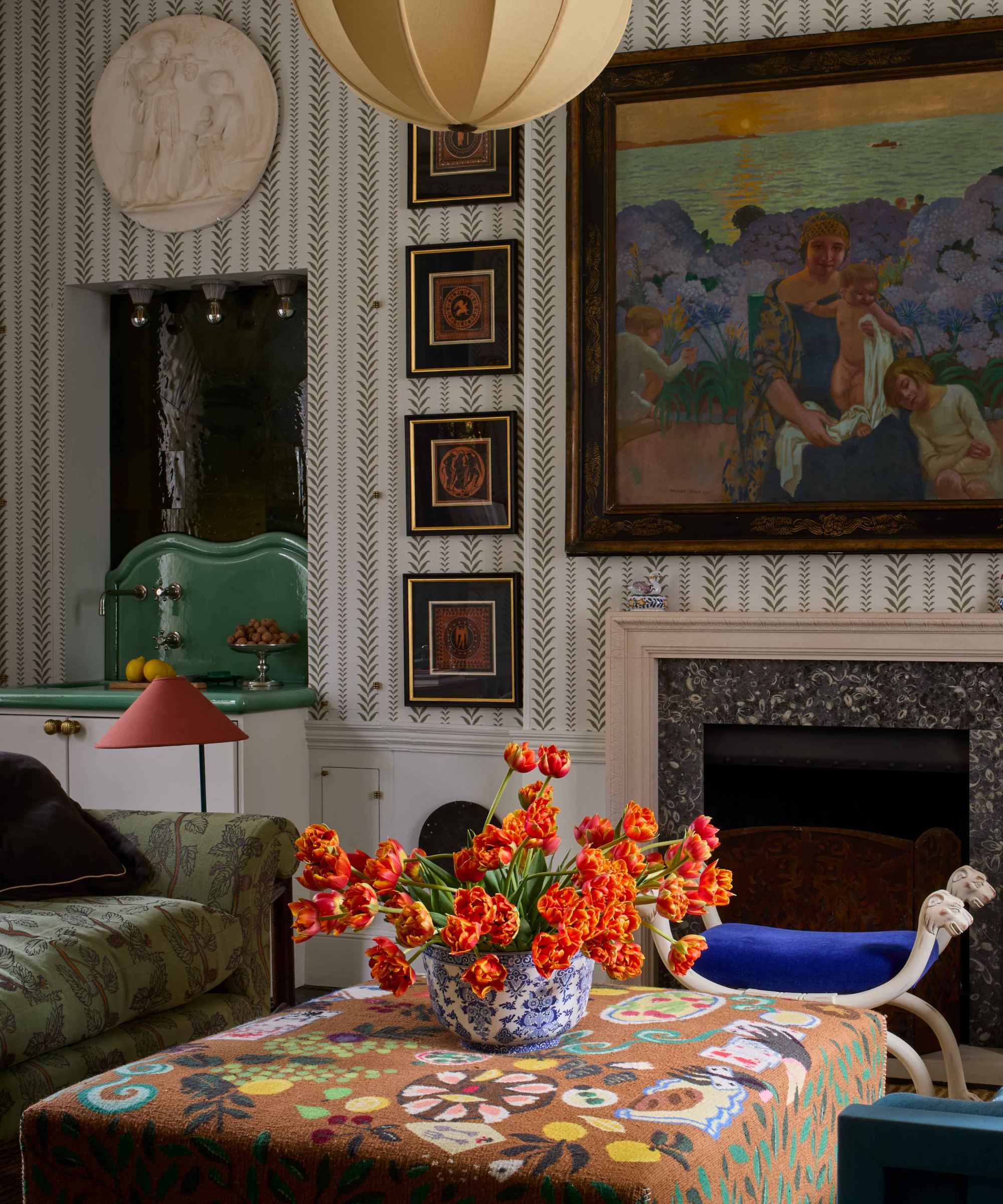 a colorful living room with lots of hanging artwork and a vase of orange flowers on the ottoman