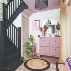 A white hallway with a pink shoe storage cabinet and a round wall mirror hung above it
