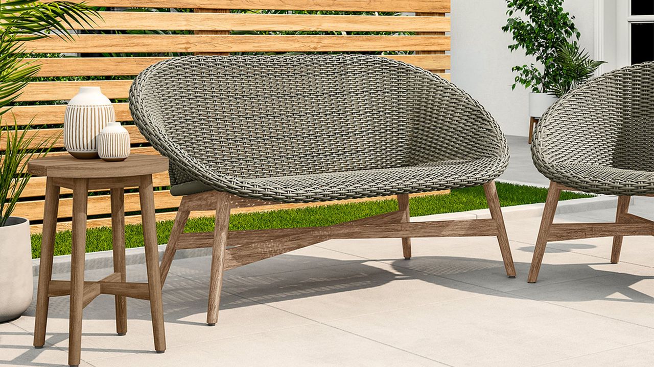 Grey rattan outdoor sofa with wooden table on a cream patio 