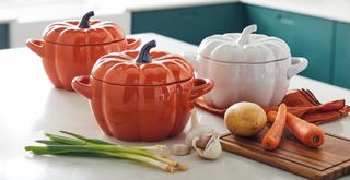 teal kitchen with white countertops with three Aldi pumpkin casserole dishes in orange and white with spring onions, garlic, potato and carrot ingredients on a wooden chopping board