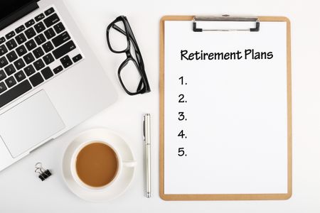 clipboard that says "retirement plans" and a checklist with a computer, glasses, and other desk items