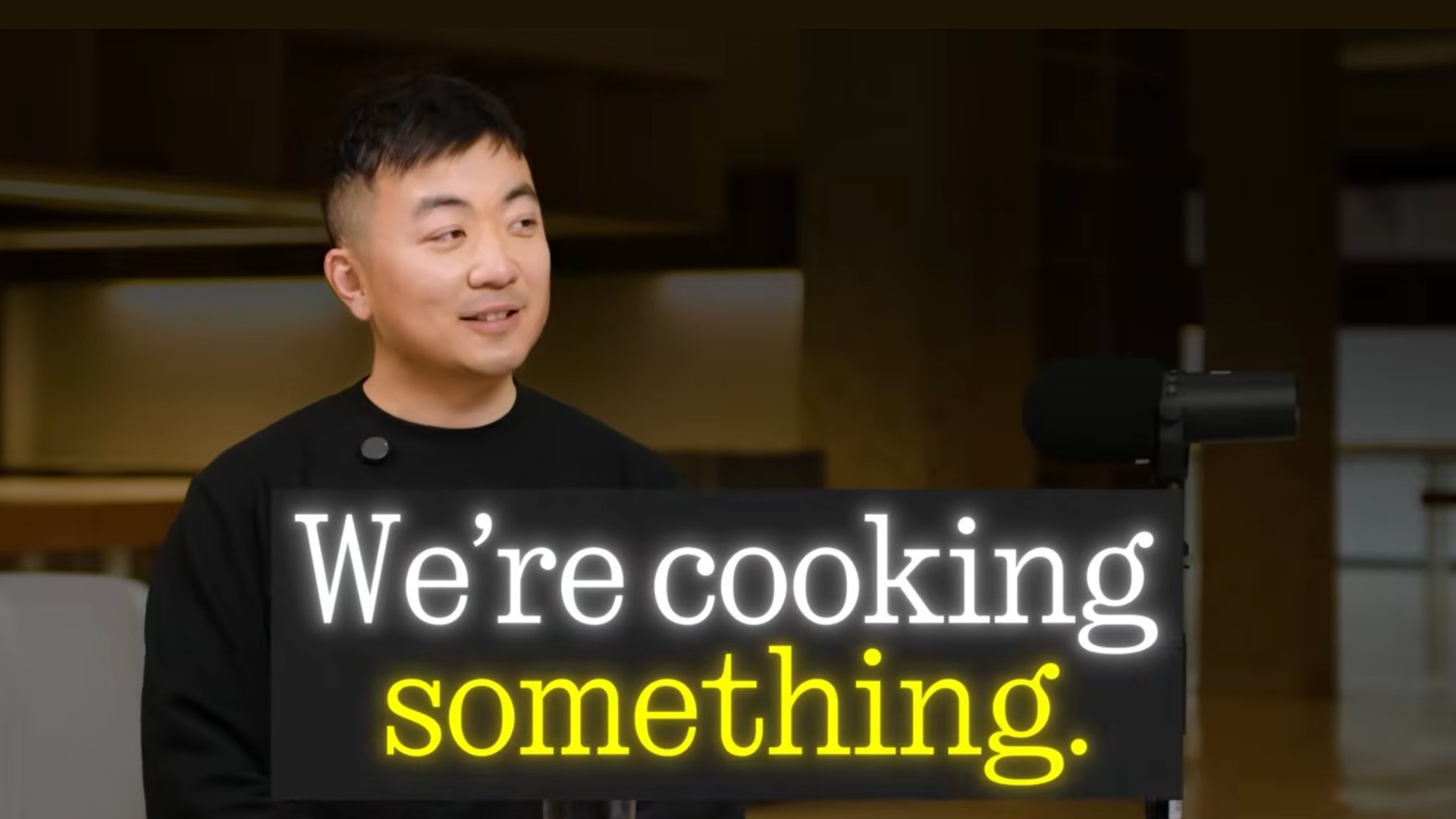 Carl Pei, CEO of Nothing, looks off-camera with a slight smile in a studio setting, overlaid with the text &amp;quot;We're cooking something.&amp;quot;