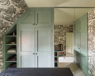 Pale green fitted storage in a box room with toile wallpaper.