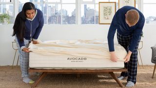 A woman and a man pull the Avocado Green Mattress Protector over a mattress