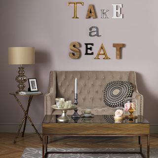 A pink living room with small button back sofa wooden coffee table and wall-mounted letters artwork