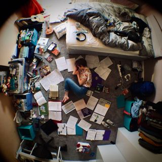 Birds-eye view of a person lying in a bedroom surrounded by books and paper