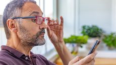 An older man wearing glasses looks closely at his smartphone.