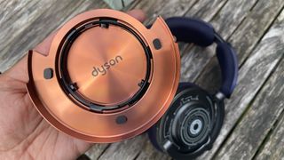 Dyson OnTrac wireless headphones on wooden table with earcap in hand showing logo