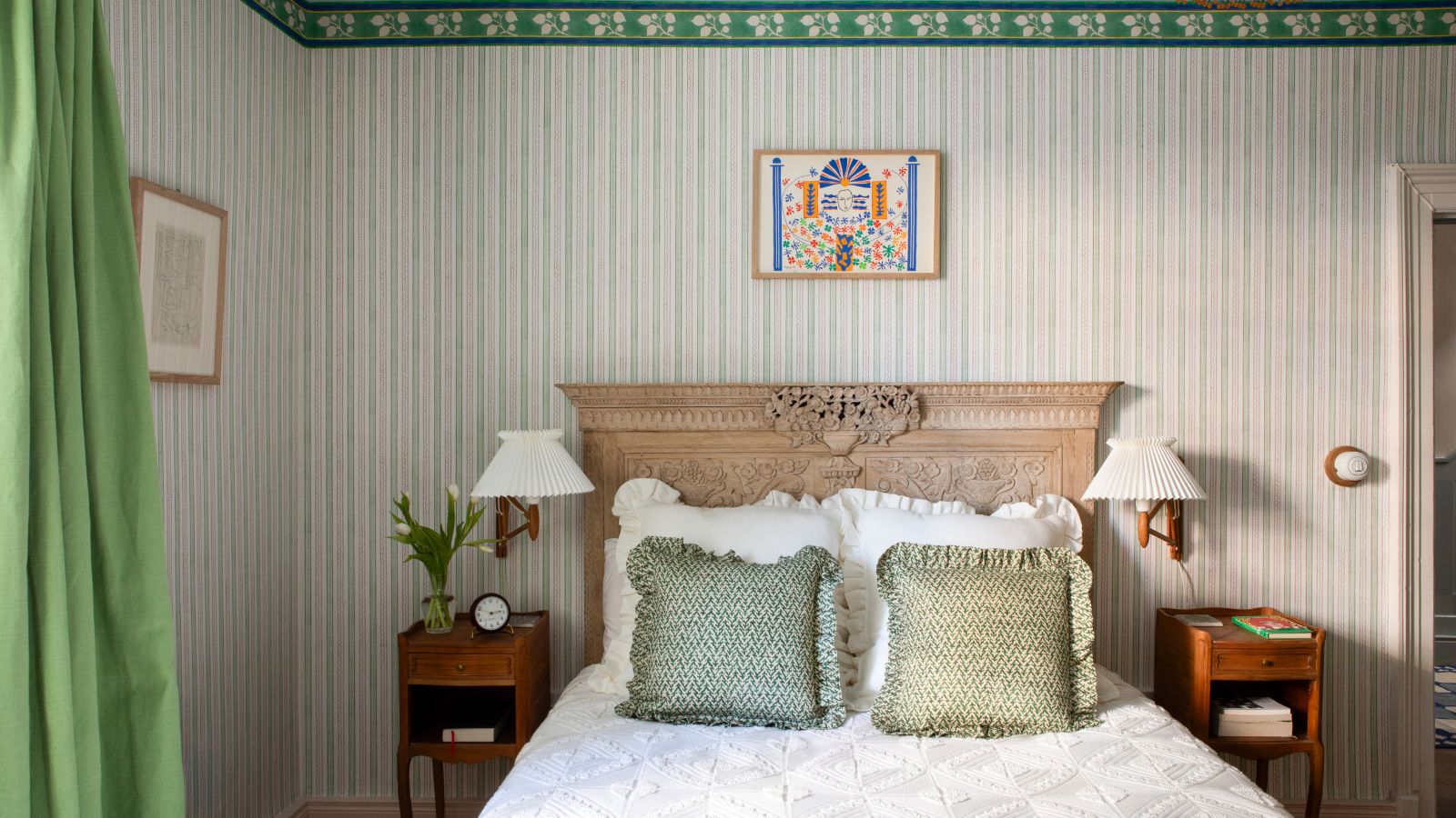 Bedroom with striped green wallpaper, green curtains and a wooden carved headboard