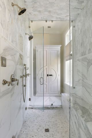 Marble-clad walk-in shower with view through to tall white cupboard