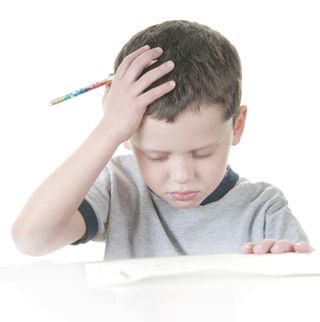 A little boy works on school work, with a look of frustration on his face.