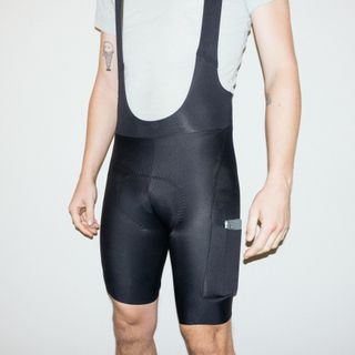 A white man wears a set of cargo bib shorts against a white background