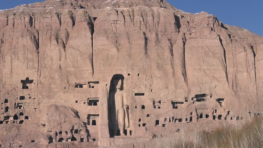 A massive statue of Buddha carved into a sandstone cliff.