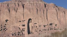 A massive statue of Buddha carved into a sandstone cliff.