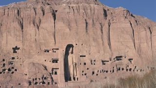 A massive statue of Buddha carved into a sandstone cliff.