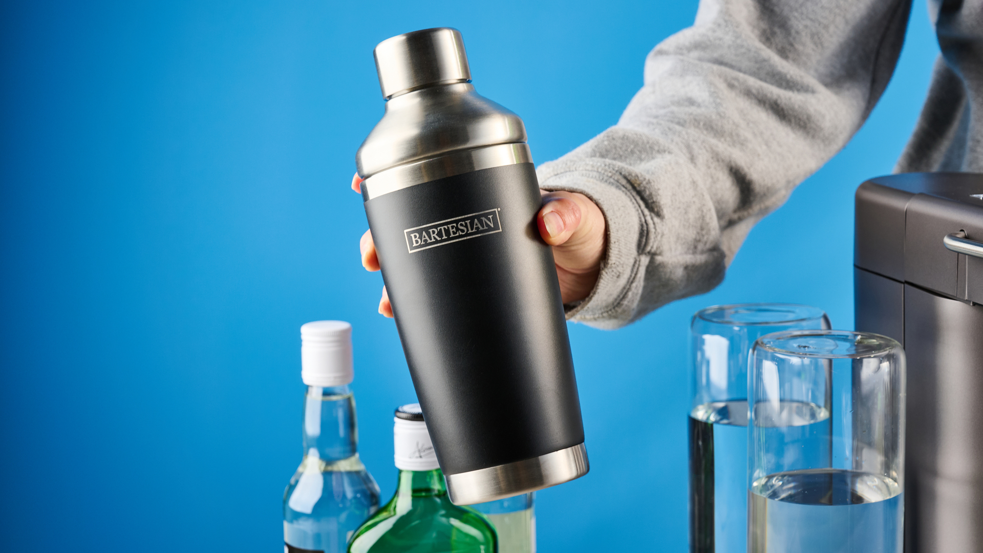 the bartesian premium cocktail machine photographed against a blue background showing its drink-making abilities and accessories and functionality with cocktail pods