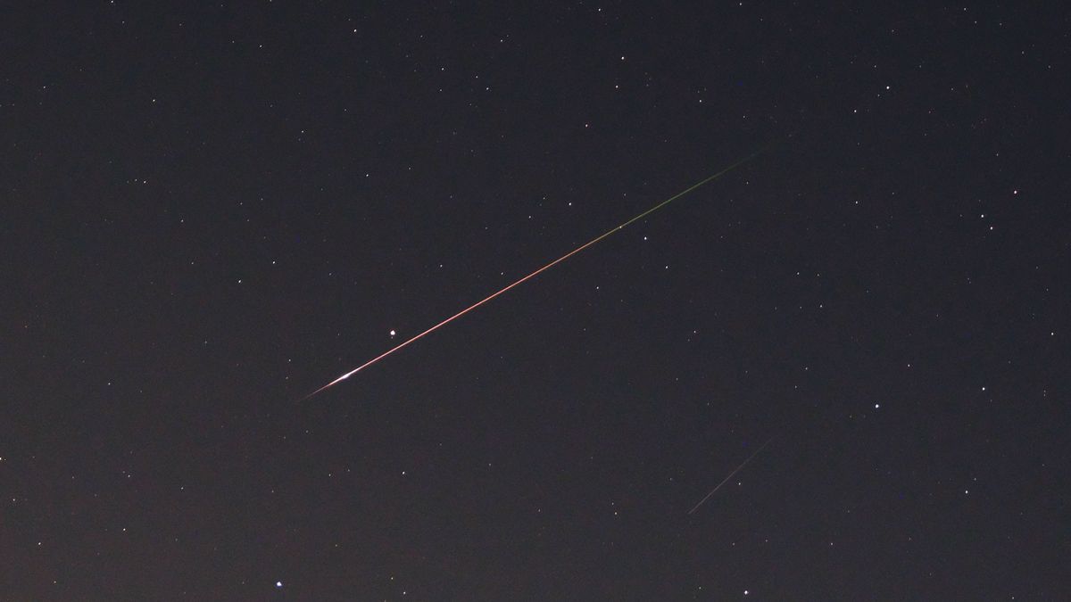 A Perseid meteor strikes through the starry night sky with a orange and green streak, as photographed by the Fujifilm GFX100S II.