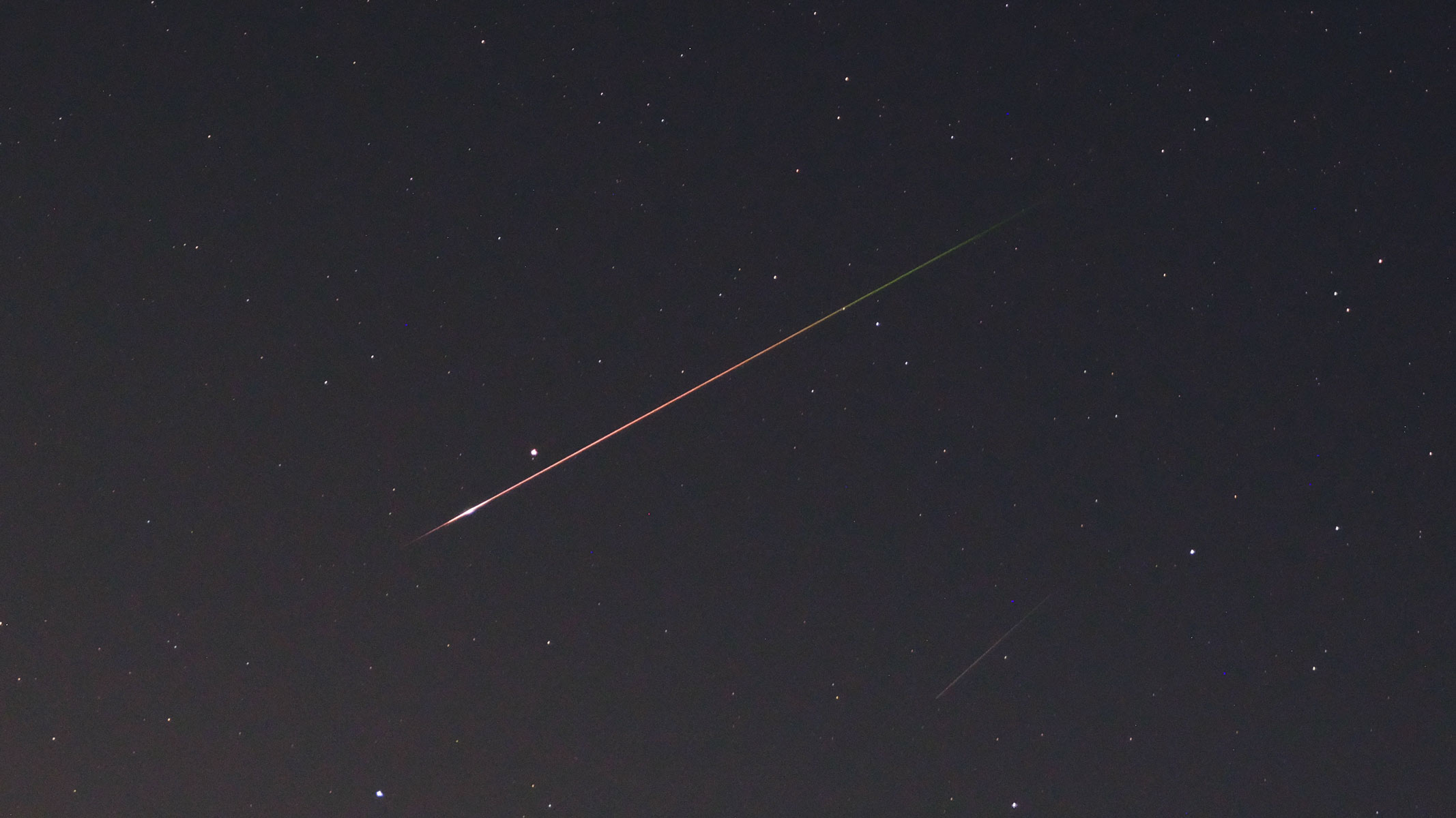 A Perseid meteor strikes through the starry night sky with a orange and green streak, as photographed by the Fujifilm GFX100S II.