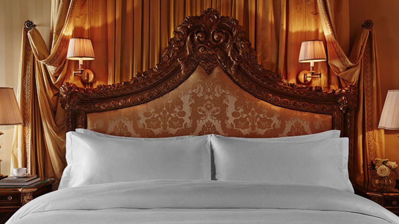 Frette bed sheets on an ornate bed frame against a gold curtain.