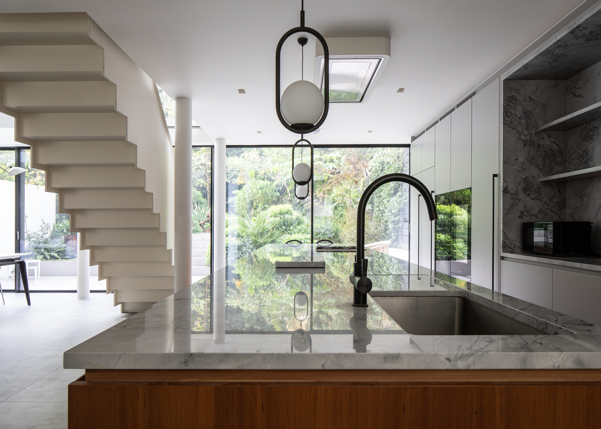 An open plan kitchen with a large island, floor-to-ceiling windows, and a large staircase