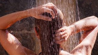 A woman is seen washing her hair in a hot shower