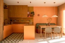 Warm-toned open-plan kitchen and dining room with orange cabinetry, oak cabinets, patterned floor tiles, woven dining chairs, and soft pendant lights