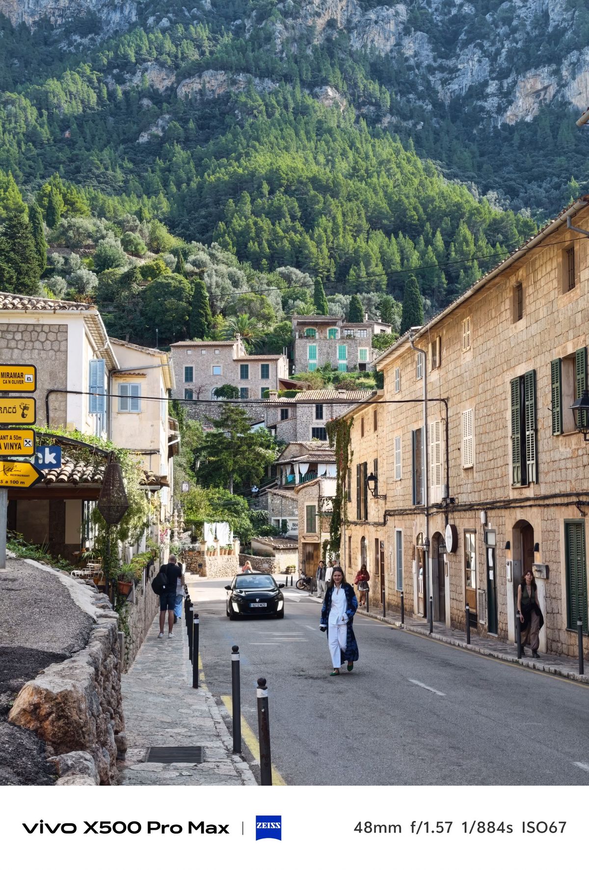 Stone village street leading toward houses and a steep forested mountain.