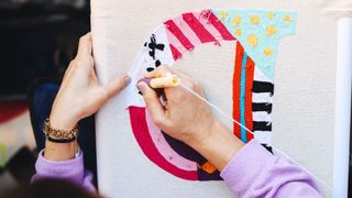 A lady makes a punch needled letter D on canvas