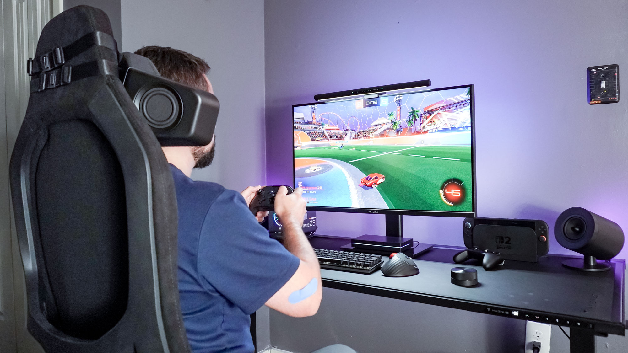 A person sitting at a desk playing Rocket League on PC with the Razer Clio wireless speaker head cushion in surround sound mode paired with the Razer Nommo V2 speakers