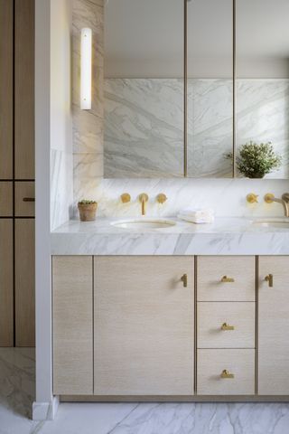 A bathroom vanity with a marble worktop and storage and mirrors above