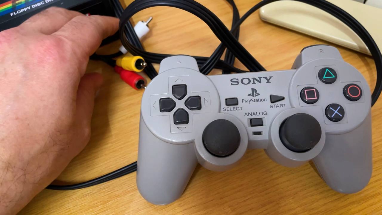 PlayStation PUGA PS1 plug and play prototype controller on desk with hands reaching for built in composite cables.