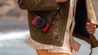 Panasonic Lumix S9 camera in red on a strap against a persons brown jacket