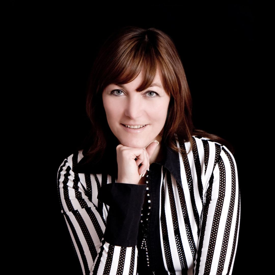Headshot of a woman with brown hair resting her chin on her hand, she is wearing a black and white striped shirt with a black collar 