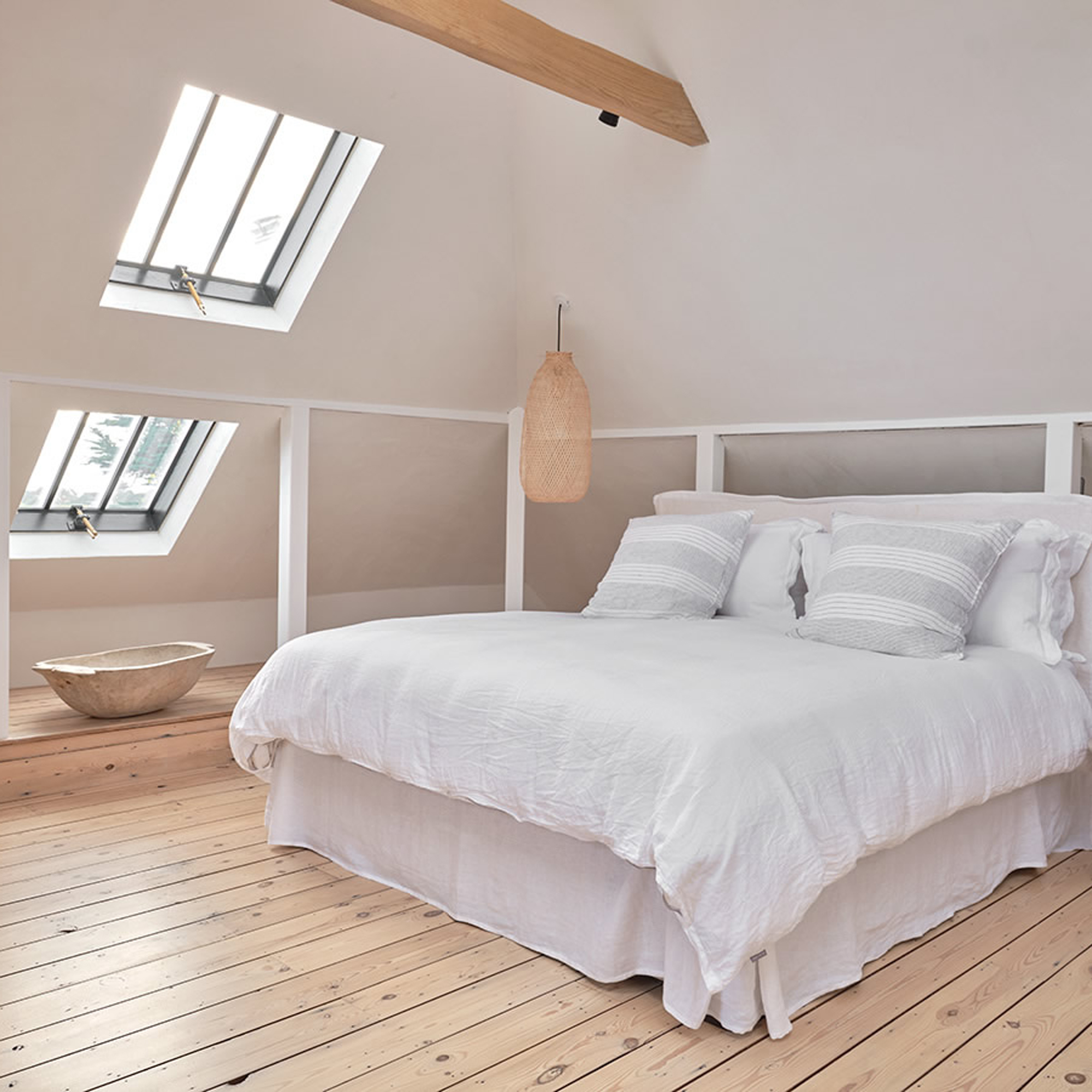 a sparely decorated bedroom with pale white walls, white bed linen and wooden floorboards