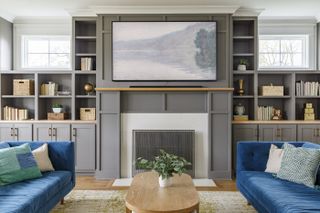 A living room with grey built-in shelving, a fireplace, and two blue sofas facing each other