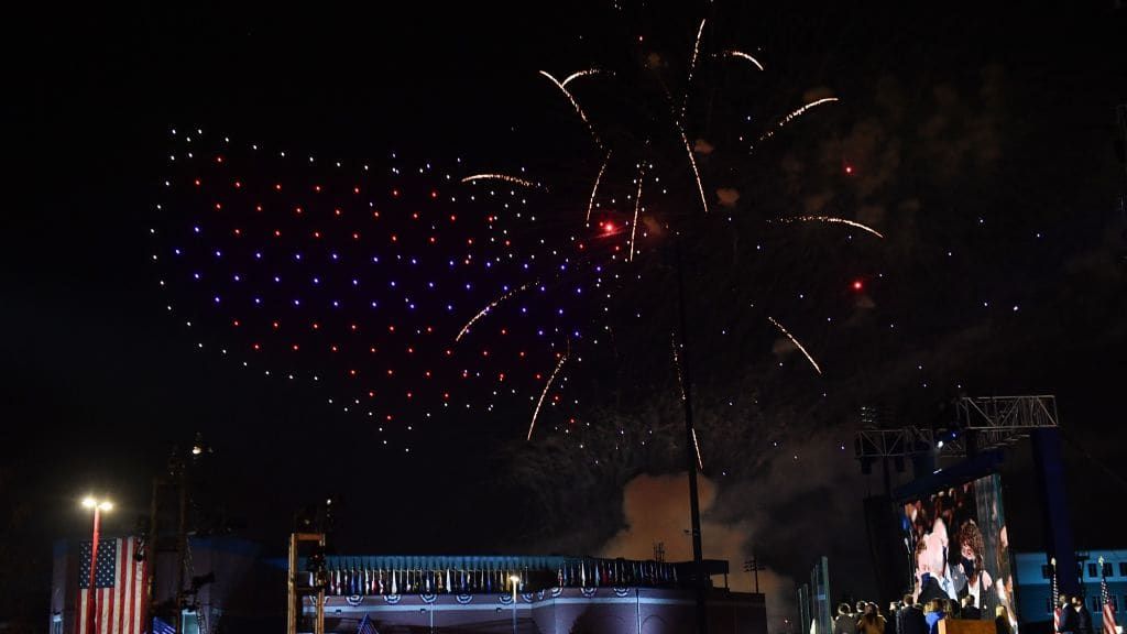 Fireworks go off next to drones creating the shape of the United States.