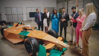 The Apprentice candidates gather round a brightly coloured orange and green racing car.