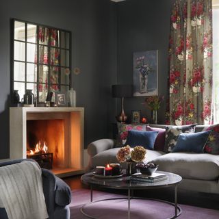 A dark living room with purple-painted walls, floral curtains and a fire place