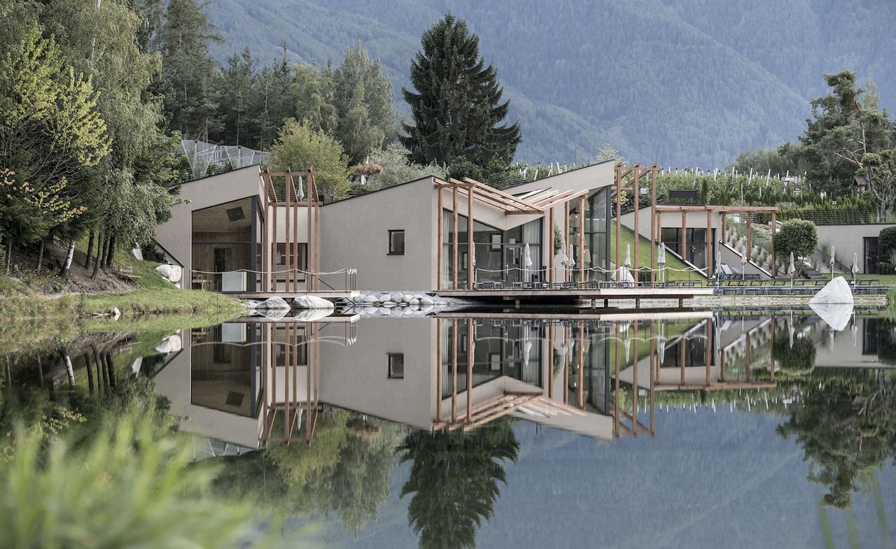 Exterior view of the Seehof Nature Retreat, Italy surrounded by greenery. The reflection of the retreat can be seen in the lake