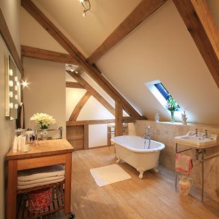 bathroom with sloping roof bathtub yellow lights and wooden flooring