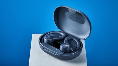 the jlab go sport+ earbuds photographed against the blue tom's guide background, showing charging case and wearing style
