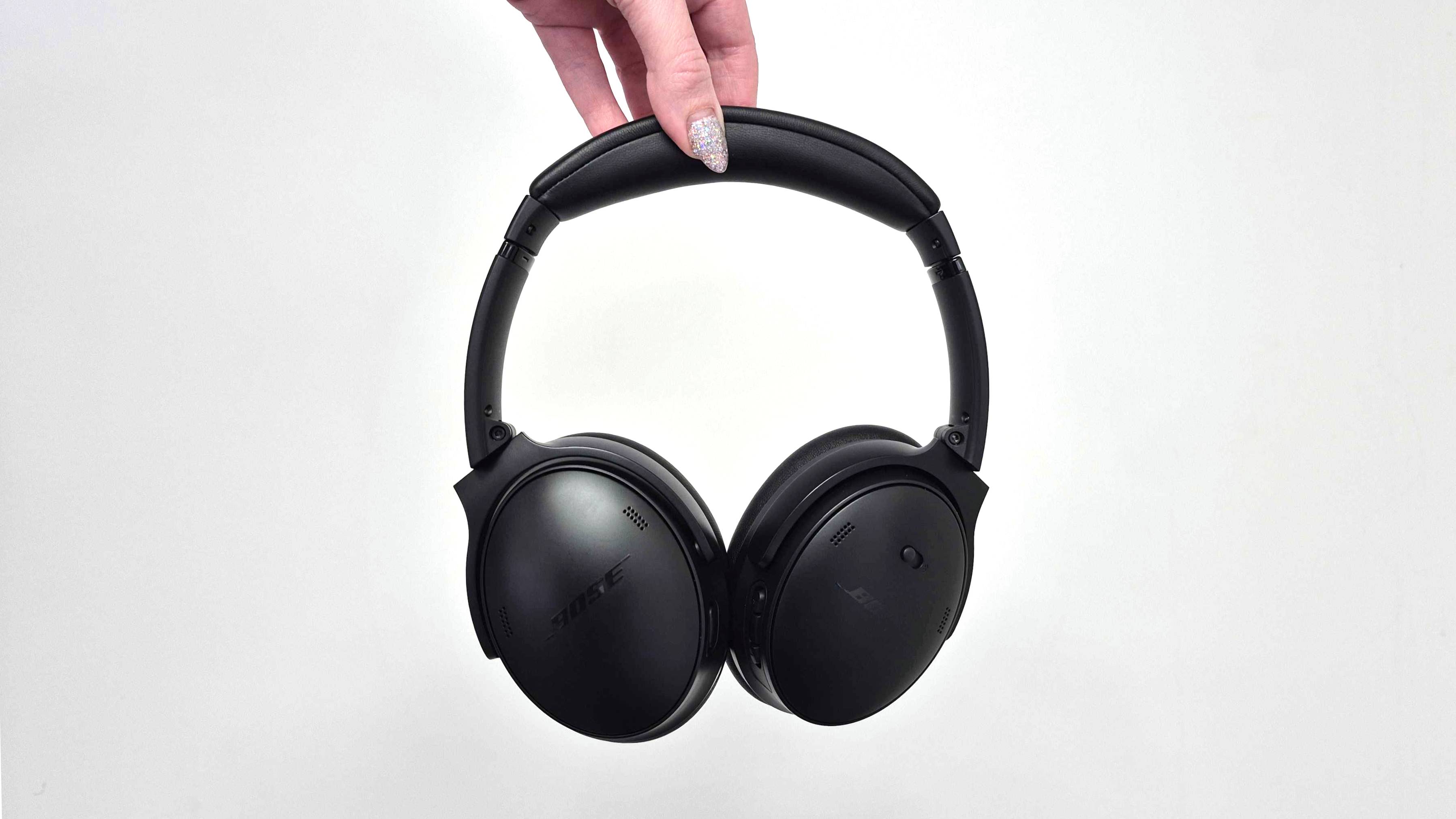 A pair of black Bose QuietComfort headphones are being held up in front of a white background.