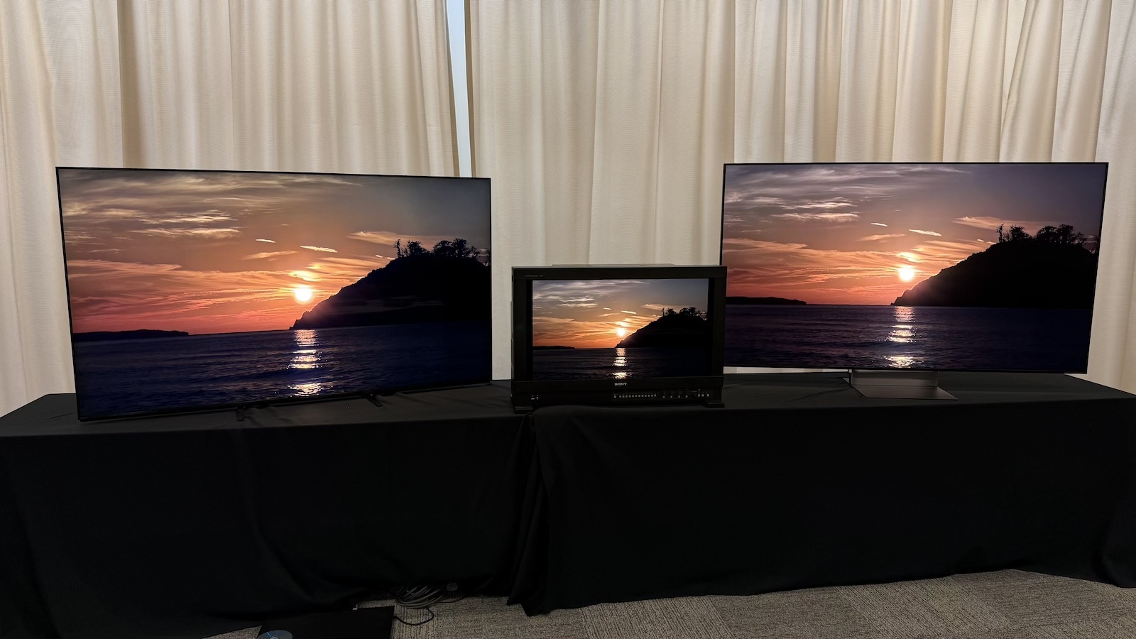 The Sony Bravia 9 II and Bravia 9 TVs, and the Sony BVM-HX3110 mastering monitor, photographed on a black desk, with Sony demo footage on the screens