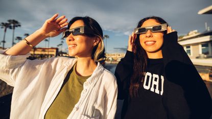 two women looking at the sun wearing solar eclipse glasses
