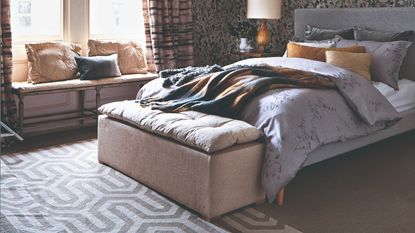 A bedroom with a grey bed frame and fluffy bedding with a patterned grey rug laid down at the foot of the bed